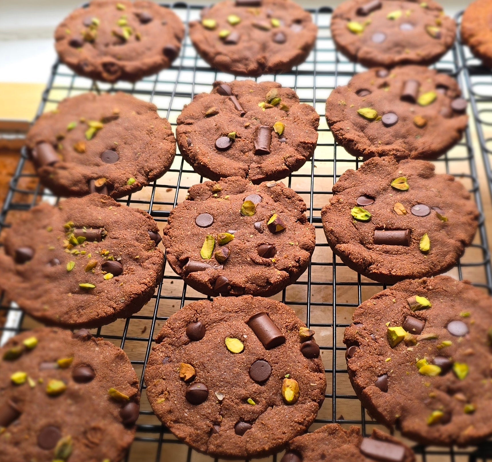 Chocolate cookies with chocolate chips and pistachios on a cooling rack.