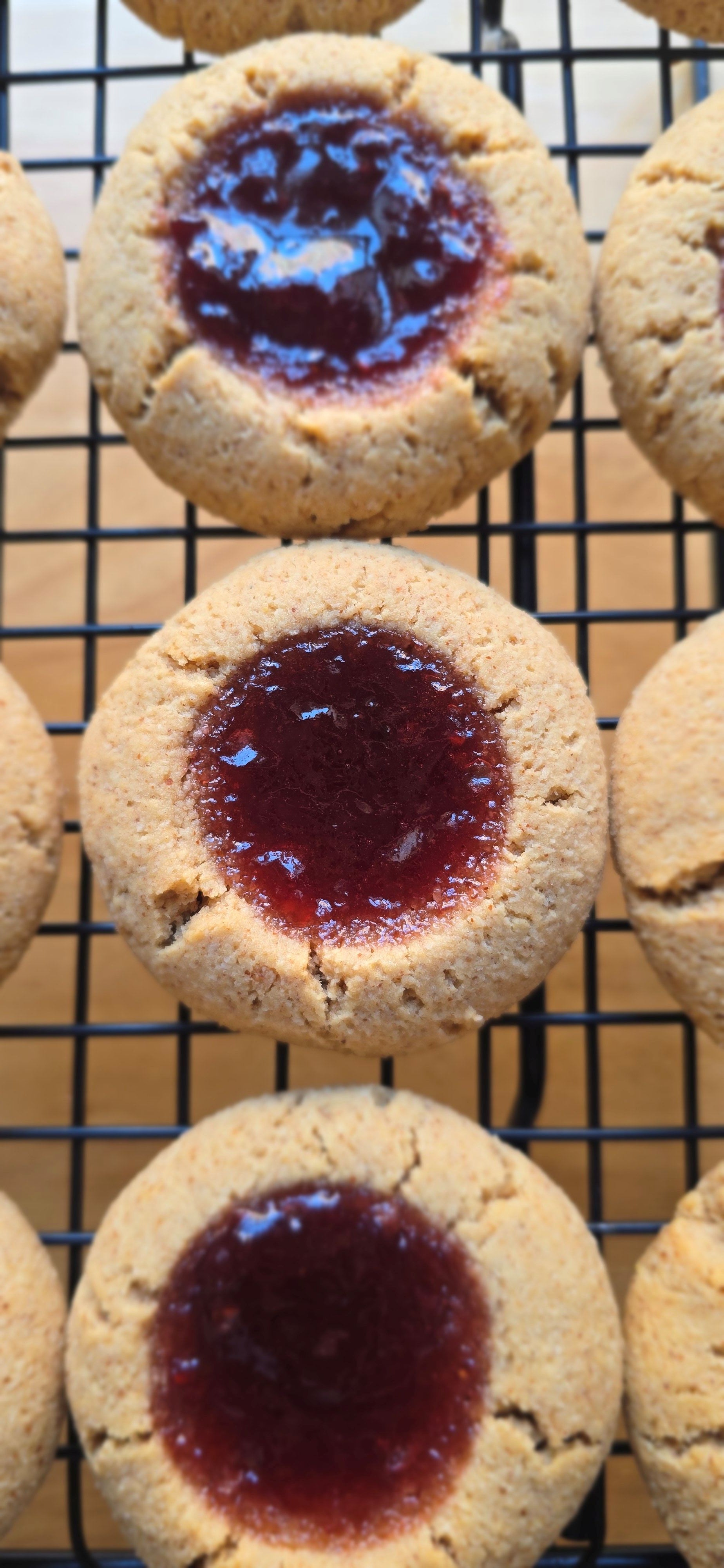 a close up of 3 almond cookies with jelly filling on a cooling rack