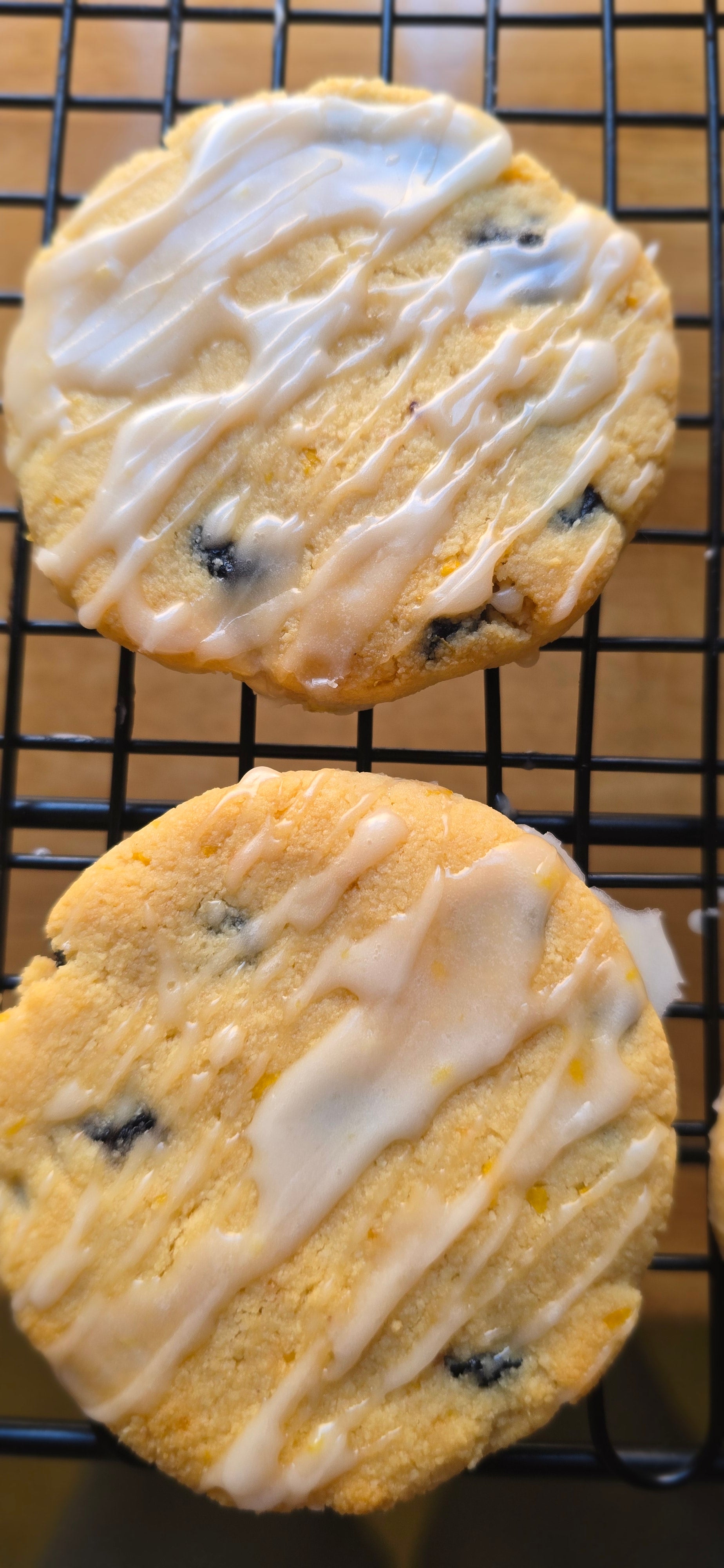 Two iced cookies with blueberries on a cooling rack.
